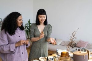 Two women trying perfume next to a table.